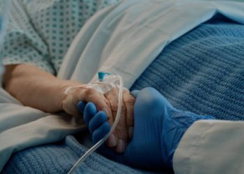 Gloved hand holding the hand of a cancer patient receiving IV treatment