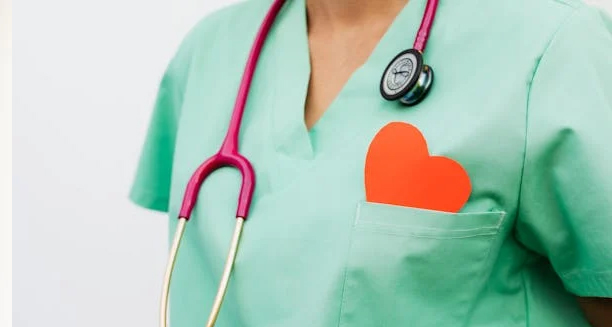 Healthcare worker in scrubs with a stethoscope and red heart shape in pocket