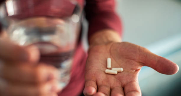 Person holding white capsules and a glass of water, preparing to take medication for cellulitis