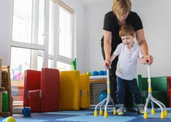 Child receiving physical therapy with walking aids and therapist in a playroom