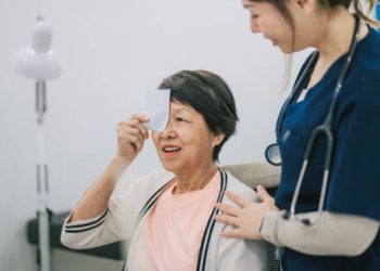 Elderly woman undergoing eye test with a nurse assisting her