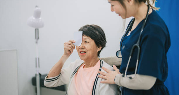 Elderly woman undergoing eye test with a nurse assisting her