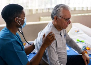 Healthcare worker examining elderly man's lungs with stethoscope