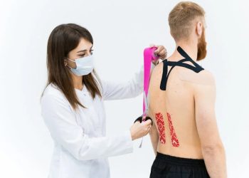 Healthcare professional applying kinesiology tape to a patient's back during spinal injury rehabilitation