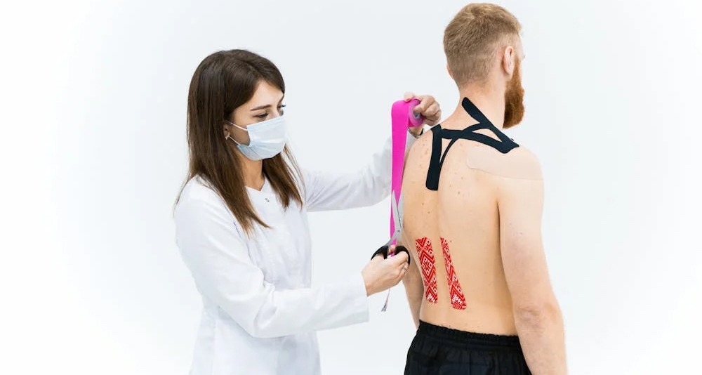 Healthcare professional applying kinesiology tape to a patient's back during spinal injury rehabilitation