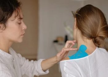 Physiotherapist applying kinesiology tape to a woman's shoulder for collarbone treatment