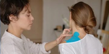 Physiotherapist applying kinesiology tape to a woman's shoulder for collarbone treatment