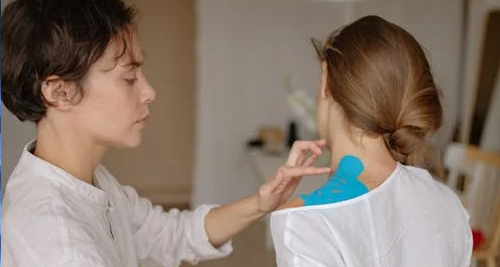 Physiotherapist applying kinesiology tape to a woman's shoulder for collarbone treatment