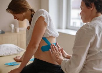 Physiotherapist applying kinesiology tape on a woman’s back for broken rib treatment