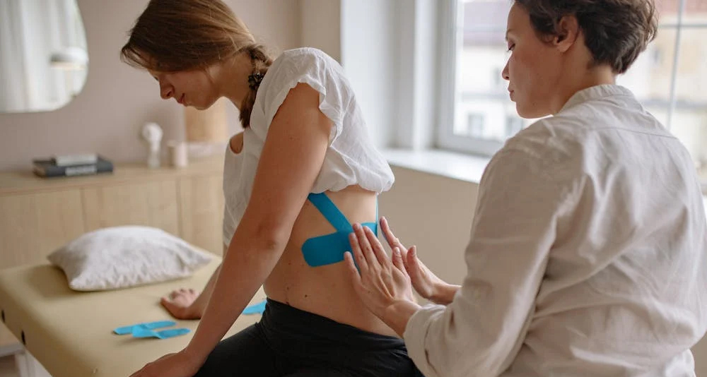 Physiotherapist applying kinesiology tape on a woman’s back for broken rib treatment