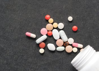 Various pain relief tablets and capsules spilled from a bottle on a black surface