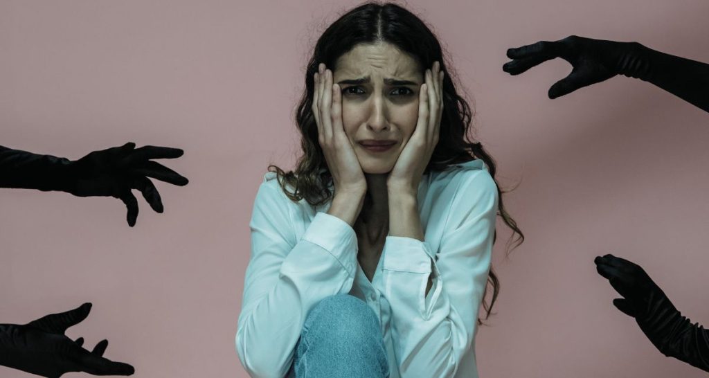 Anxious woman surrounded by black-gloved hands symbolising panic attack triggers