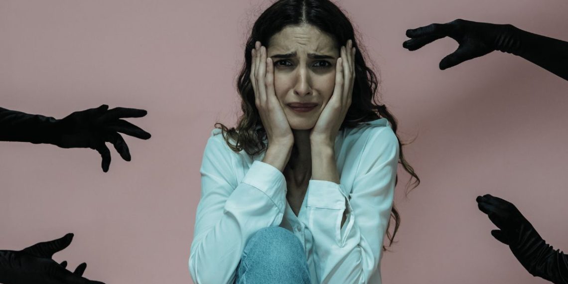 Anxious woman surrounded by black-gloved hands symbolising panic attack triggers