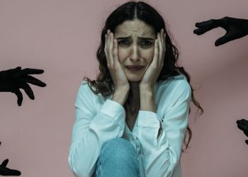 Anxious woman surrounded by black-gloved hands symbolising panic attack triggers