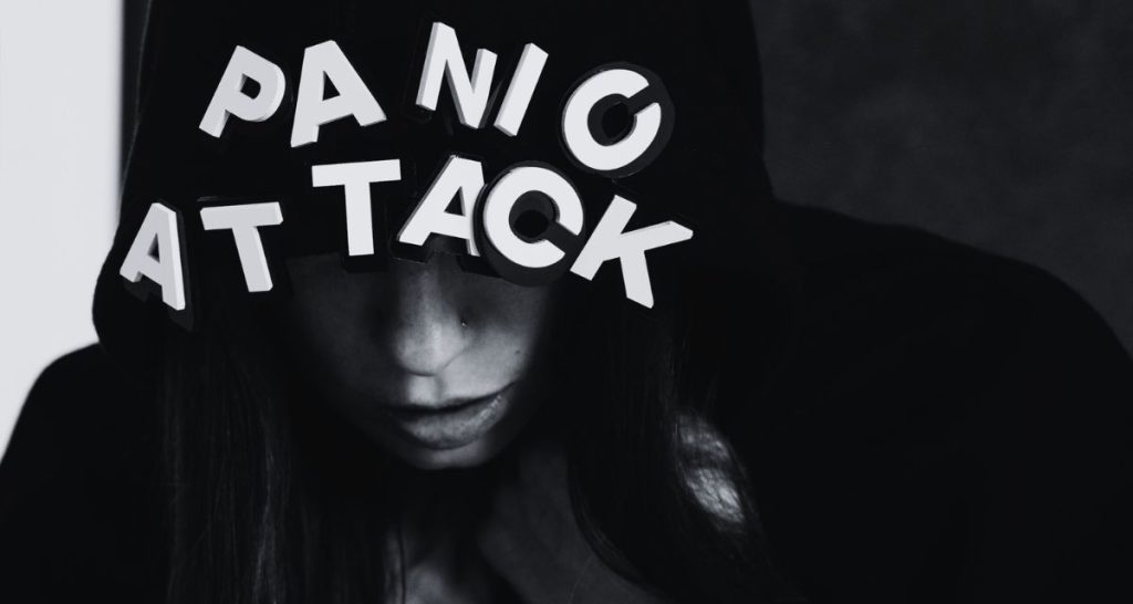 Woman in hoodie overwhelmed by the words “Panic Attack” above her head