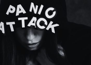 Woman in hoodie overwhelmed by the words “Panic Attack” above her head