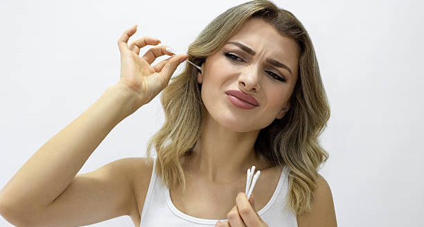 Woman using cotton swab in ear with discomfort, indicating poor ear hygiene