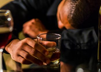 Man holding a glass of alcohol with his head down, illustrating alcohol as a cause of chronic pancreatitis.