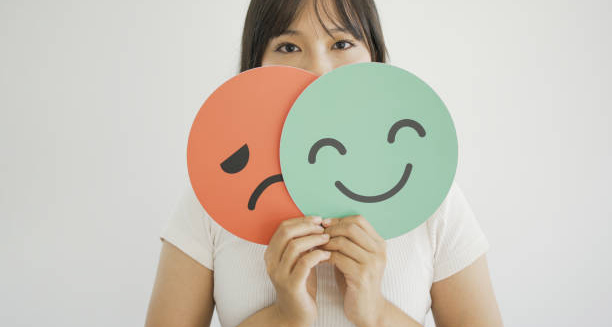 Woman holding smiling and frowning face icons in front of her mouth