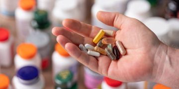 Hand holding various pills and capsules, indicating medication as a possible cause of constipation.