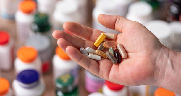 Hand holding various pills and capsules, indicating medication as a possible cause of constipation.