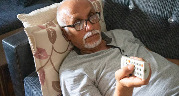 Elderly man lying on a couch with a remote control, symbolising inactivity as a risk factor for coronary heart disease.
