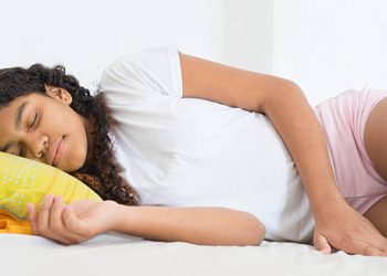 Young girl lying in bed, possibly experiencing early puberty symptoms