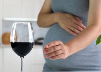Pregnant woman reaching for a glass of red wine, highlighting the cause of Fetal Alcohol Spectrum Disorder