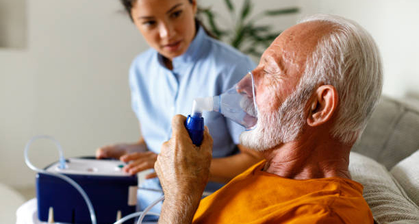 Elderly man with COPD using a nebuliser at home, assisted by a nurse.