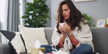 Woman wrapped in a blanket suffering from the common cold at home