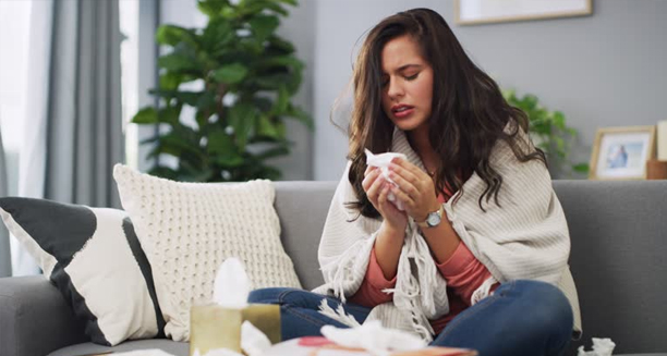 Woman wrapped in a blanket suffering from the common cold at home