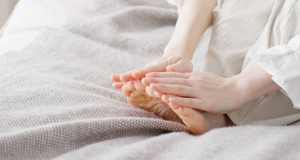 Person gently touching feet affected by chilblains while resting in bed
