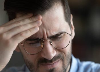 Man in glasses grimacing with pain and holding his forehead during a cluster headache