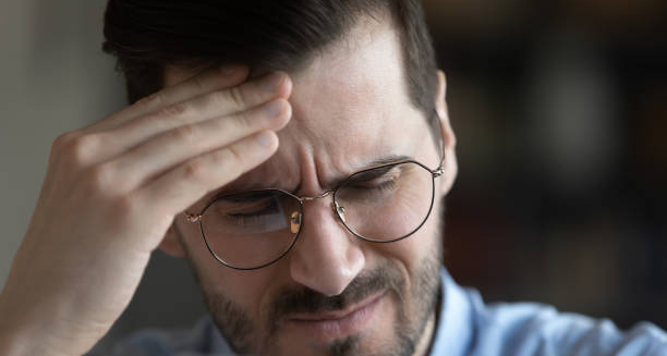 Man in glasses grimacing with pain and holding his forehead during a cluster headache