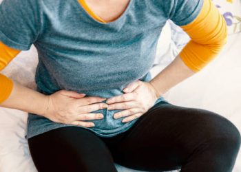 Woman clutching stomach in pain while sitting on a bed