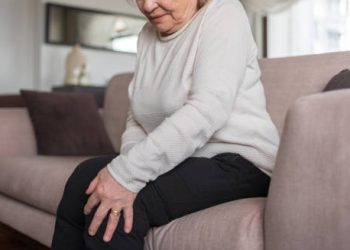 Elderly woman sitting and holding her painful knee in discomfort