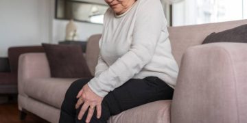 Elderly woman sitting and holding her painful knee in discomfort