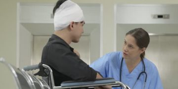 Nurse speaking with a male patient in a wheelchair wearing a head bandage after concussion