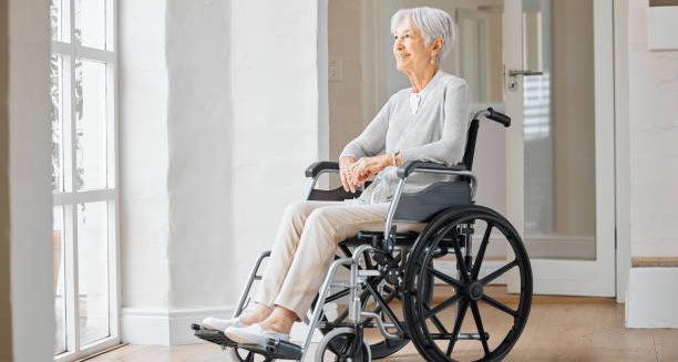Elderly woman in a wheelchair looking out a window, symbolising mobility challenges related to corticobasal degeneration.