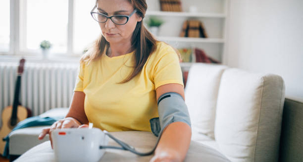 Woman in a yellow shirt measuring her blood pressure at home, reflecting ongoing health monitoring after Cushing’s syndrome.