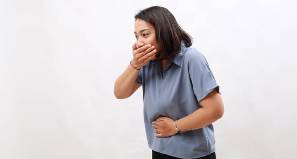 A woman clutching her stomach and covering her mouth, showing signs of nausea and discomfort, which may indicate a vomiting episode.