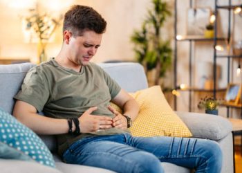 Man sitting on a couch, holding his stomach in discomfort due to abdominal pain.