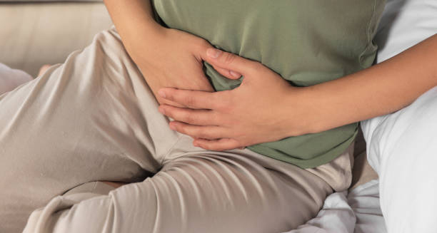 Person holding their lower abdomen while sitting, indicating pelvic discomfort due to cystitis.