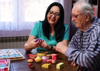 Elderly man receiving cognitive therapy with caregiver using colourful memory toys