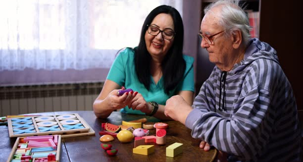 Elderly man receiving cognitive therapy with caregiver using colourful memory toys