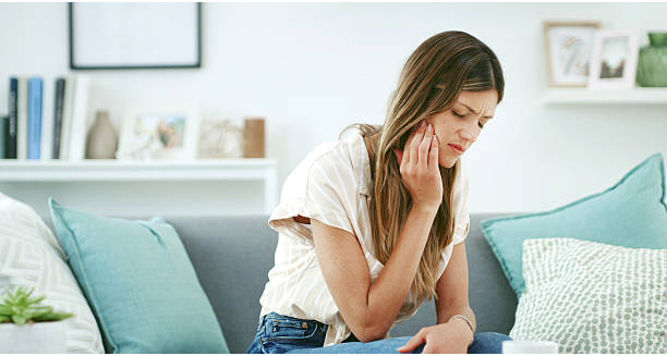 Woman holding jaw in pain while sitting on a couch