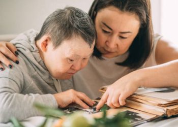 Woman supporting an adult with Down’s syndrome while looking through a photo album