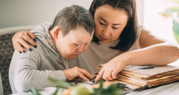 Woman supporting an adult with Down’s syndrome while looking through a photo album