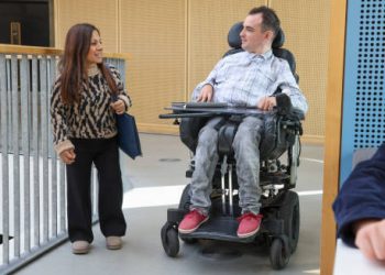 Woman with dwarfism and man in wheelchair talking in a modern building