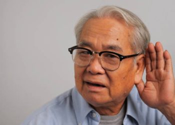 Elderly man holding hand to ear indicating hearing difficulty